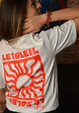 Remera blanca de algodón con estampa roja en la espalda que incluye el texto "LE SOLEIL" y un sol estilizado.