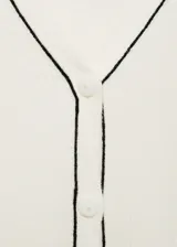Cárdigan negro de punto de canalé con cuello pico, cierre frontal con botones y ribete blanco en cuello, botones y borde de la abertura.