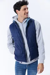 Chaleco acolchado azul marino con cierre frontal y cuello alto. Reversible, con interior en tono celeste. Sin mangas.
