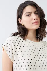 Blusa color crudo con estampado de puntos negros, de corte recto y manga corta.