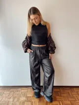 Pantalón negro de ecocuero suave, corte ancho, con bolsillos delanteros y elástico en la cintura.