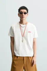 Camiseta blanca de corte recto, cuello redondo y manga corta. Estampado pequeño en el frente y estampado grande en la espalda con texto en color rojo.