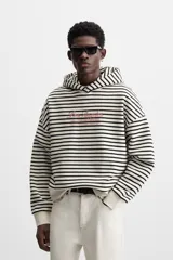 Sudadera con capucha a rayas horizontales blancas y negras, corte boxy fit, mangas largas y texto bordado en color rosa en el pecho.