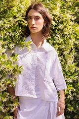 Camisa blanca de lino bordado, corte amplio y largo cropped, con cuello clásico y bolsillo frontal.