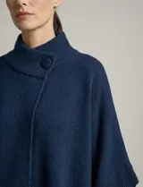 Capa o poncho tejido color verde esmeralda, con cuello polera alto que se cierra con un botón grande en el lateral. Presenta mangas cortas estilo japonesa y un calce amplio.