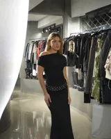 Vestido largo negro de corte ajustado, con escote asimétrico y cinturón con apliques metálicos.