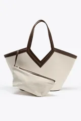 Bolso tipo shopper color crudo, con cuerpo de lona y detalles en cuero marrón. Tiene doble asa de hombro y una bolsa interior extraíble con cierre de cremallera. Se cierra con un lazo.