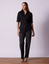 Camisa negra de algodón con cuello clásico, escote en V y mangas 3/4 con trabillas y lazos. Tiene dos bolsillos con solapa en el pecho y cierre frontal con botones.