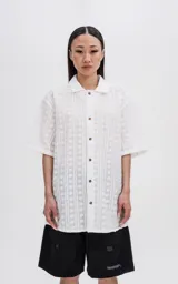 Camisa blanca con textura y botones marrones, de corte holgado y mangas cortas.