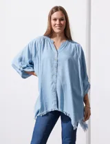 Camisa celeste de tencel, corte amplio, con cuello mao, escote en V y abotonadura frontal. Tiene bolsillos aplicados en el pecho, mangas 3/4 regulables con presilla y ruedo desflecado.