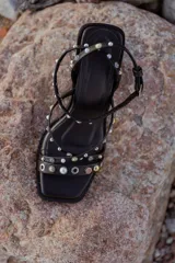 Sandalias negras con tiras finas adornadas con apliques metálicos y perlas. Taco de 9 cm y base cuadrada.