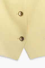 Chaleco amarillo pálido con cuello cuadrado, tirantes finos, falsos bolsillos de vivo y cierre frontal con botones.
