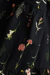 Vestido largo de algodón negro con estampado de flores pequeñas en tonos rosa y amarillo. Tiene cuello mao, mangas globo cortas, cinturón fino extraíble y falda acampanada con fruncido escalonado.