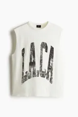 Musculosa blanca de algodón con cuello redondo y sisas sin rematar. Estampado negro con la palabra 'L.A.C.A' en el frente. Corte holgado.