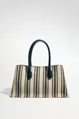 Bolso tipo shopper de mano confeccionado en canvas color beige con rayas verticales negras. Tiene tira interior con cierre de mosquetón metálico, bolsillo interior con cierre de cremallera metálica y cierre imantado.