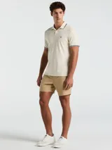 Polo color crema con cuello clásico, mangas cortas y logo bordado en el pecho. Presenta detalles de doble línea en cuello y mangas.