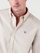 Camisa lisa color beige de algodón, con cuello abotonado, corte regular y manga larga terminada en puño simple.