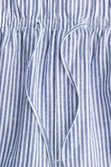 Pantalón tobillero de corte holgado en tejido liviano de mezcla de lino a rayas verticales azules y blancas. Modelo de tiro alto con elástico revestido y cordón para ajustar fino en la cintura, bolsillos al bies y piernas ajustadas.