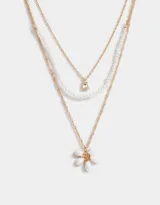 Collar corto multicadena dorada con una cadena de eslabones, una de perlas y una de eslabones con dije de flor blanca.