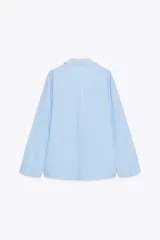 Camisa oversize celeste con textura de algodón, cuello solapa y manga larga. Presenta pliegues delanteros y bajo asimétrico.