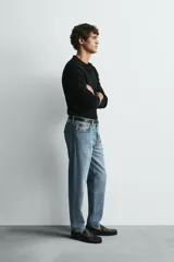 Jeans de denim de algodón, color negro lavado, con tiro medio, corte ajustado en cadera y muslos, y pierna que se estrecha hacia el tobillo. Presenta cinco bolsillos y cierre frontal con cremallera y botón.