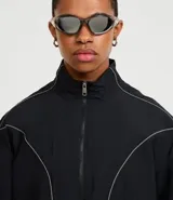 Campera deportiva negra con cuello alto, cierre frontal de cremallera y elásticos en puños y bajo. Presenta recortes geométricos definidos por costuras en hilo reflectante.