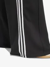 Pantalón de sudadera Adidas de corte ancho, color negro con tres rayas blancas verticales en los laterales y logo bordado en la parte superior. Confeccionado en tejido de felpa francesa.