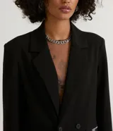 Blazer negro de poliéster y viscosa, de corte alargado, con cuello solapa, manga larga, doble botón frontal y bolsillos con solapa.