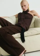 Conjunto de dos piezas color marrón oscuro, compuesto por un top asimétrico de un solo hombro con un pañuelo integrado que cae como bufanda, y un pantalón de vestir de tiro medio, corte recto y pierna ancha.