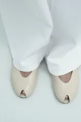 Zapato plano destalonado color beige, con punta abierta, tira trasera con elástico ajustable y suela a contraste de color. Acabado en punta redonda.