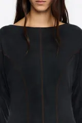 Vestido de largo midi en color negro con corte en línea A y vuelo. Posee escote barco, mangas largas tipo murciélago ajustadas en los puños y detalles de pespuntes decorativos a contraste. Está confeccionado en una mezcla de cupro y elastano.