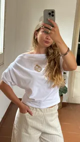 Remera blanca de algodón con cuello tipo bote y detalle de elástico en los hombros, creando un efecto de caída asimétrica.