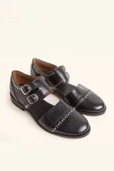 Zapato tipo monk strap con aberturas laterales, confeccionado en cuero vacuno color bordó. Presenta doble tira con hebillas metálicas plateadas en el empeine y suela de cuero con taco bajo.