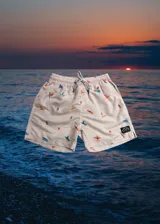Short de baño color rosa claro con estampado de motivos playeros: personas haciendo surf, palmeras y ananás. Tiene cintura elástica con cordón ajustable.