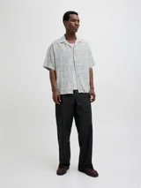 Camisa de manga corta Jack & Jones con cuello resort y calce amplio. Presenta un estampado integral de motivos náuticos y abstractos en tonos azul chambray y beige. Confeccionada en una mezcla de viscosa y lino, ideal para climas cálidos.