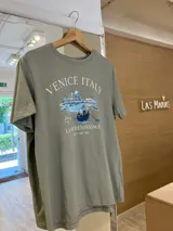 Remera verde oliva de algodón jersey con cuello redondo y mangas cortas. Estampado frontal con la leyenda "Venice Italy", una ilustración de la ciudad de Venecia y la frase "La Serenissima Est. 421 AD".
