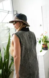 Vestido corto de jean gris con botones frontales, sin mangas, con cuello camisero y bolsillos en el pecho.