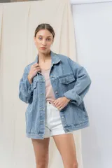 Campera denim celeste de corte oversize, con cuello clásico, cierre frontal con botones metálicos, bolsillos delanteros con solapa, bolsillos laterales y mangas largas con puños abotonados.