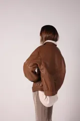 Campera bomber negra de cuero sintético con cuello de corderito blanco, cierre frontal con cremallera y botones a presión, bolsillos laterales y puños y cintura elastizados.