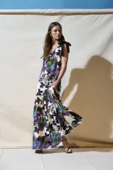 Vestido largo de corte holgado con estampado tropical en tonos violeta, verde y azul sobre fondo claro. Presenta breteles con lazos negros, escote en V y falda con volado en el ruedo.