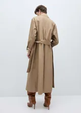 Abrigo largo color beige con cuello camisero, cierre frontal con botones, lazo ajustable en la cintura, trabillas, bolsillos laterales y forro interior.