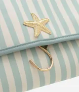 Neceser tipo hotel con estampa de rayas verticales en tonos celeste y blanco. Cuenta con asa superior, cierre con solapa y gancho metálico dorado para colgar. Decorado con aplique de estrella de mar dorada.