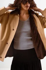 Chaqueta tipo sobrecamisa o abrigo ligero color camel, con cuello solapa de color marrón oscuro, cierre frontal de botones y bolsillos laterales.