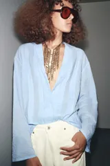 Camisa oversize celeste con textura de algodón, cuello solapa y manga larga. Presenta pliegues delanteros y bajo asimétrico.