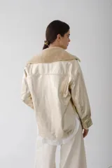 Camisa de cuero metalizado color champagne, con cuello de piel sintética color beige, cierre frontal con botones dorados, bolsillos con solapa en el pecho y corte recto.
