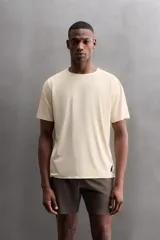 Camiseta deportiva marrón confeccionada en tejido técnico ligero y elástico con estructura perforada. Cuello redondo, manga corta y bajo asimétrico con aberturas laterales. Detalle de logo estampado.