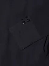 Mono largo negro con cuello y solapa, manga larga con puño de doble botón, dos bolsillos laterales y dos bolsillos de plastrón en el pecho. Cierre frontal con cartera oculta.