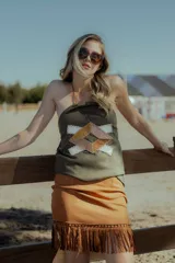 Top strapless negro confeccionado en gamuza con apliques geométricos de cuero en tonos beige y marrón. Presenta flecos en el ruedo.