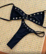 Conjunto de bikini negro con ojalillos metálicos. El corpiño es de corte triangular con tiras finas y la bombacha es tipo tanga.