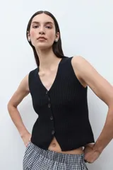 Chaleco de punto color beige melange, con escote en V y cierre frontal de dos botones oscuros. Es sin mangas y de corte ajustado.